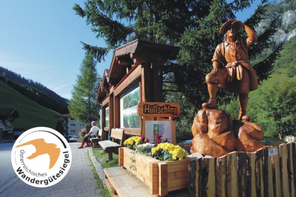 "Wander-Startplatz" im Ortszentrum des Bergsteigerdorfes Hüttschlag mit Wanderkarte, Parkplatz, Bushaltestelle und dem von Albin Kreuzer geschnitzten Bergsteiger