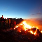 Wanderer kommen vom Tal herauf und halten Rast am Sonnwendfeuer